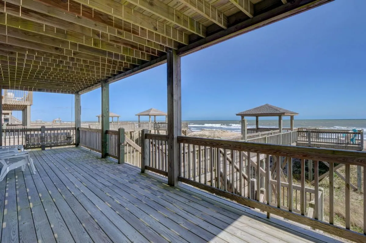 A spacious wooden deck overlooking the ocean, with gazebo structures and open space for relaxing, gathering, and watching the waves. The deck is elevated, offering clear, uninterrupted views of the shoreline.