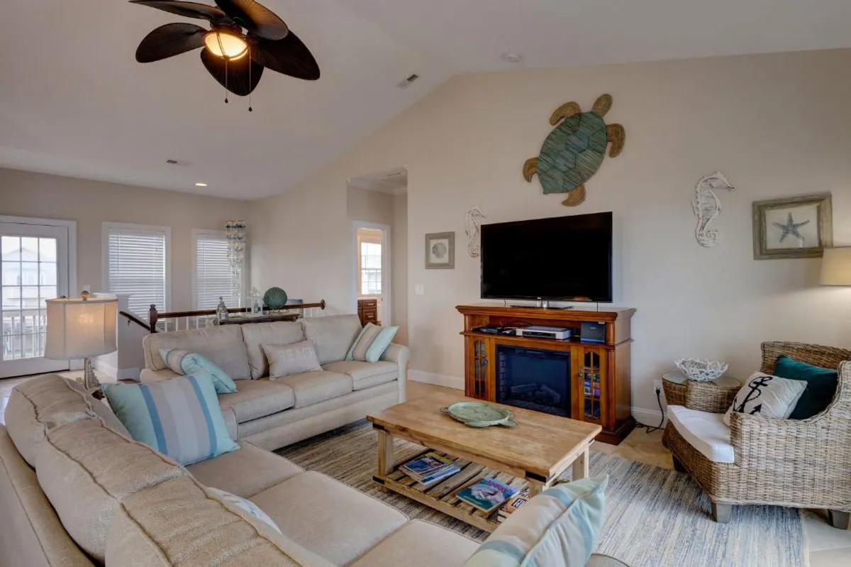 A spacious living room with a large sectional sofa, coffee table, and vibrant coastal wall art. This inviting space is designed for group socializing, offering plenty of room for friends to gather after a day at the beach.