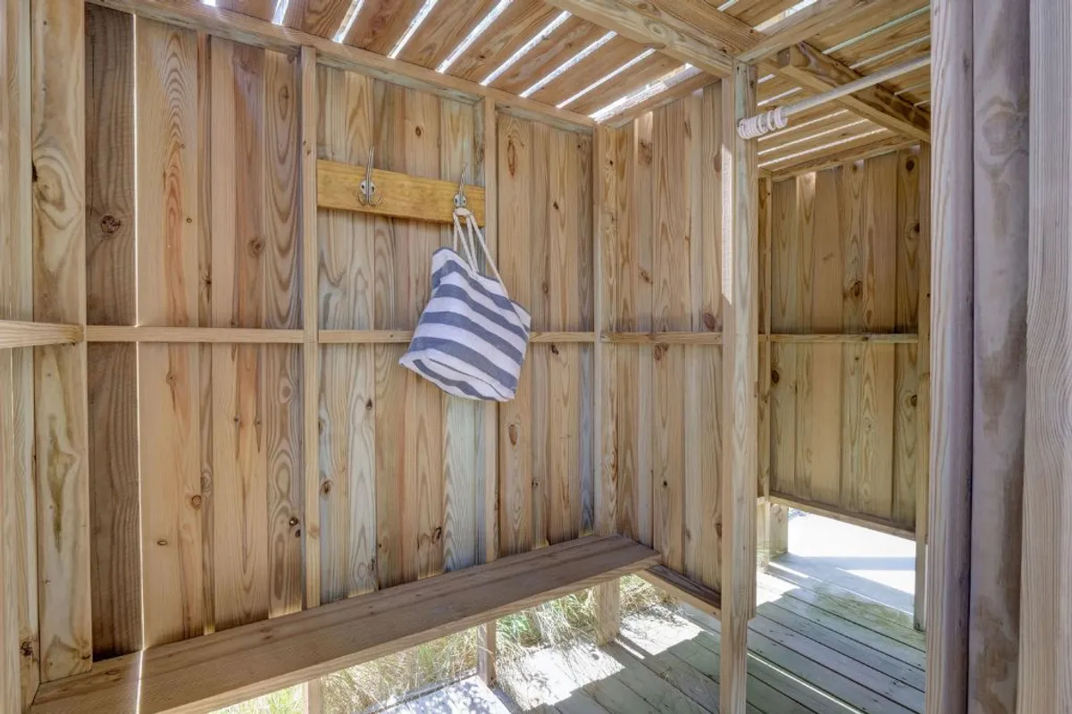 This scene shows a tranquil, wood-lined outdoor shower with an open structure, suggesting a private and refreshing spot to rinse off after a day on the beach. The setting feels serene and seamlessly blends with the coastal vibe of the home.