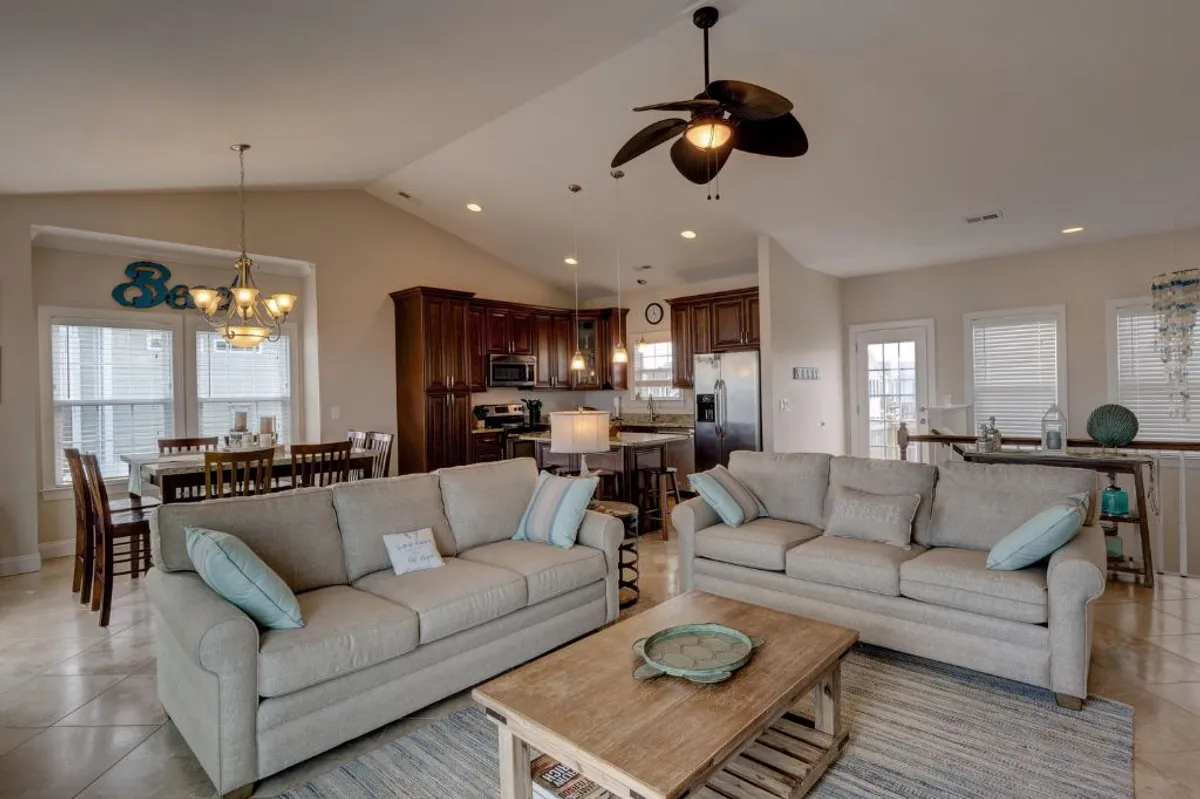 This image depicts a bright and open living space with comfortable sofas, a wooden dining table, and a visible kitchen area. The arrangement suggests a welcoming, communal environment where families or groups can relax, dine, and socialize together—all in a well-maintained setting.